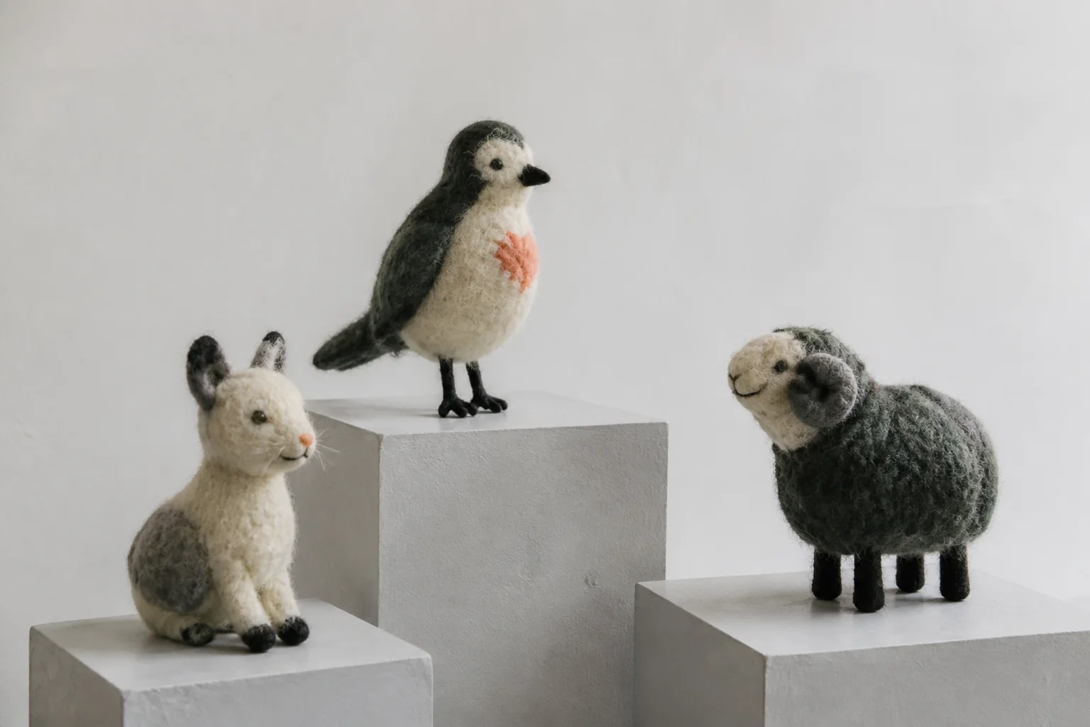 Drie handgemaakte wollen dierfiguren op lage witte sokkels