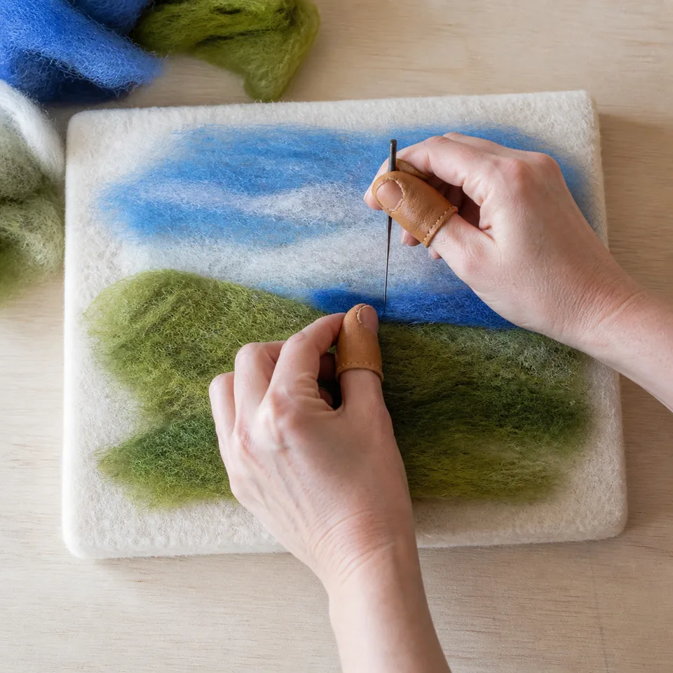 Handen die groene en blauwe wol op een vlakke ondergrond prikken